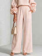 Pink wide leg pants and ruffle cuff knit top, lower body view holding a cream handbag