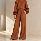 Rust knit top and wide leg pants in a sunlit room with hand in pocket